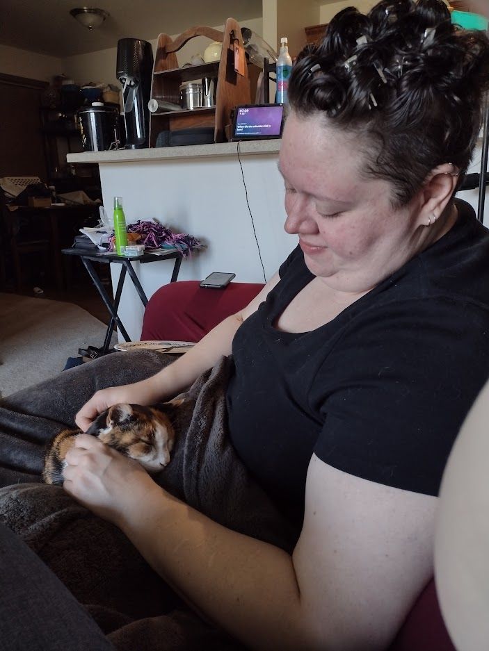 Moxie the calico cat rests in the Kate's lap, cradling her head in their hands. This is their last morning photo together.
