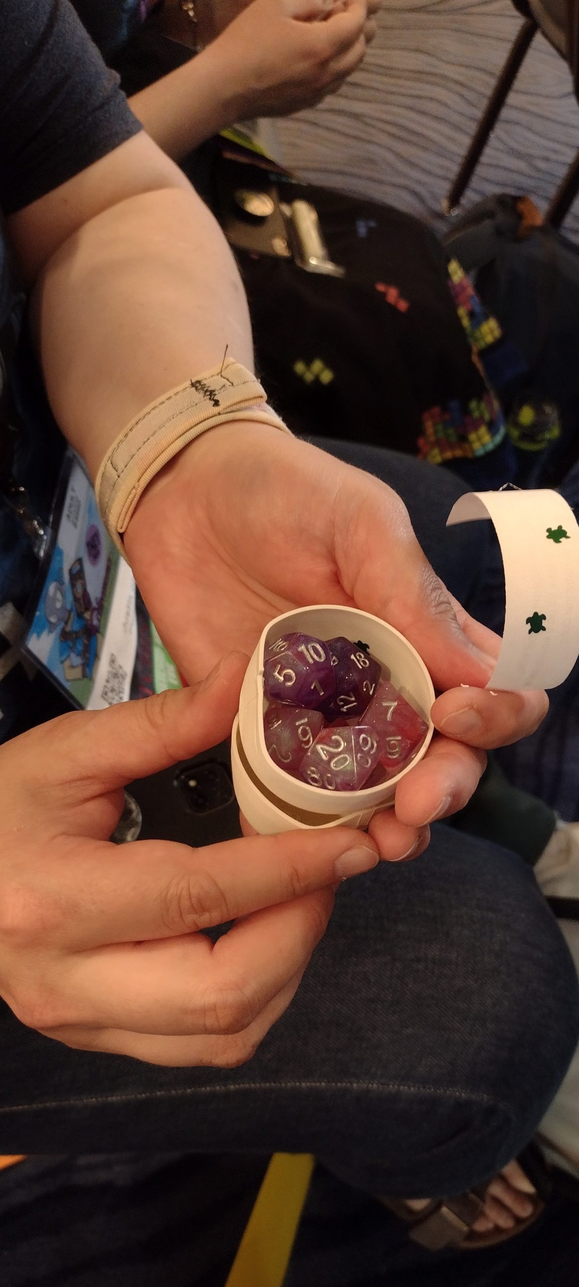 A set of purple and pink TTRPG dice sit in a half of a white eggshell that has been broken open.
