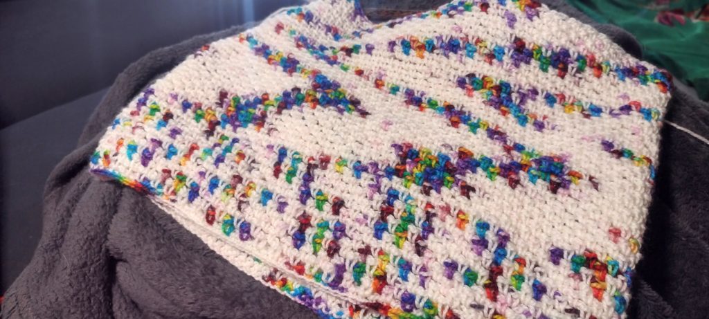 A white and rainbow variegated crocheted project. The coloring starts out very evenly spread and then begins to pool in different ways.